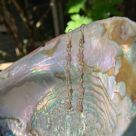 dangly gold rose quartz earrings hanging on an abalone shell